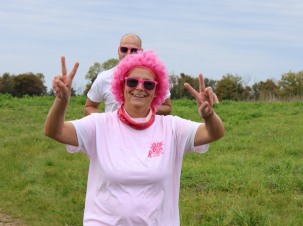Une participante en perruque et lunettes roses fait le signe de la victoire, un participant aux lunettes sombres derrière elle